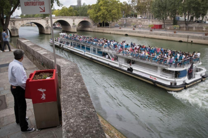 Un hombre utiliza un uritrottoir ante el paso de un bateau mouche en el Sena.-EL PERIÓDICO