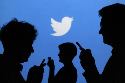 Siluetas de gente con el móvil, con el logo de Twitter al fondo.-REUTERS