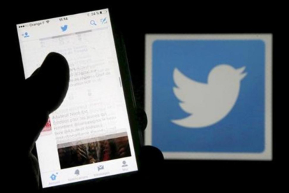 Un usuario de Twitter lee mensajes de esta red social en el móvil frente al logo del pájaro, símbolo de la misma.-/ REUTERS / REGIS DUVIGNAU