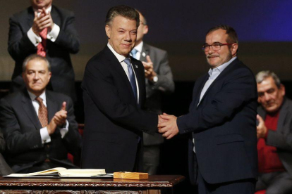 Santos (izquierda) y Rodrigo Londoño, alias 'Timochenko', se dan la mano tras firmar el nuevo acuerdo, en Bogotá, este jueves.-AP / FERNANDO VERGARA