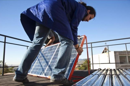 Un hombre instala placas fotovoltaicas en la cubierta de un edificio.-ARCHIVO / JOAN PUIG