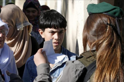 Un nino palestino muestra su carnet de identidad a una agente israelí mientras espera para poder cruzar a Jerusalen a través del puesto de control de Belén.-ABED AL HASHLAMOUN