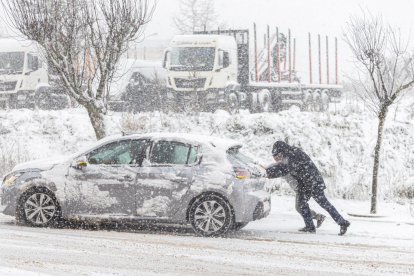Dos personas empujan un vehículo en medio de la intensa nevada.
