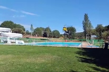 Un helicóptero carga agua en la piscina de Navaleno, previamente desalojada, para sofocar un incendio en la zona.