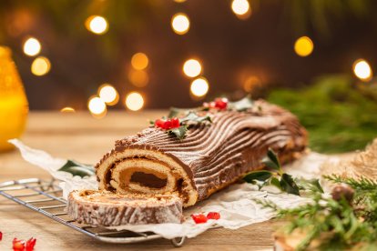 Tronco de Navidad decorado con chocolate, acebo y frutos rojos sobre mesa rústica navideña