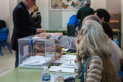 Un ciudadano introduce su voto en la urna mientras los miembros de la mesa electoral supervisan el proceso durante la jornada de votación