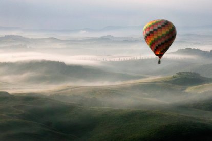 Un globo aerostático surca el cielo sobre un paisaje envuelto en niebla, evocando la experiencia única de contemplar el eclipse desde las alturas