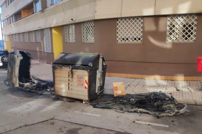 Contenedores incendiados con un vehículo afectado por el calor al fondo.
