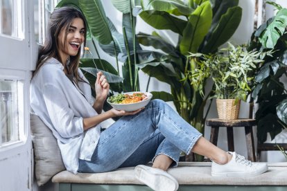 Mujer joven disfrutando de una ensalada saludable en un espacio luminoso y verde.