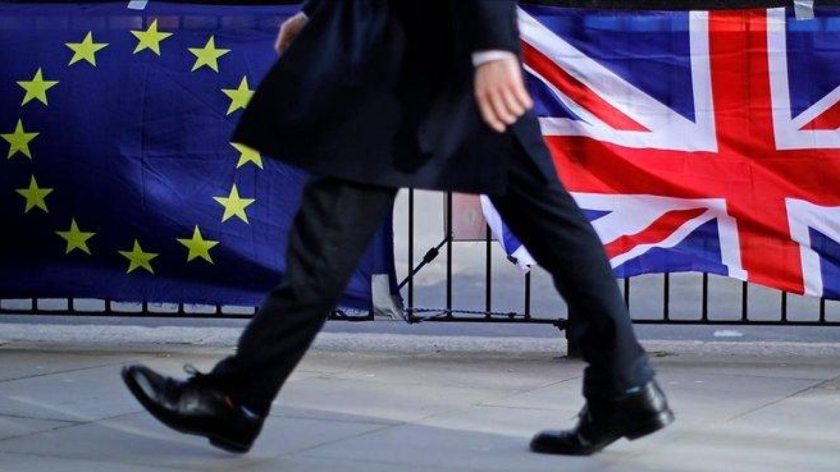 Un hombre camina junto a una bandera de la UE y otra del Reino Unido, en Londres.-TOLGA AKMEN (AFP)