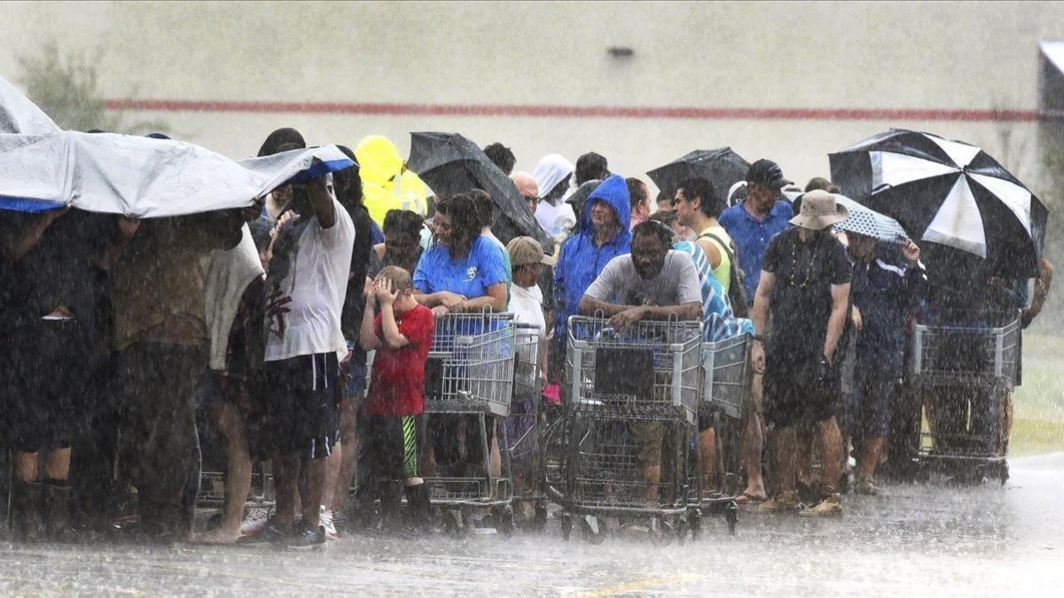 Un grupo de personas hace cola bajo una intensa lluvia en una tienda de ultramarinos en Carolina del Norte.-AP/ CHUCK LIDDY