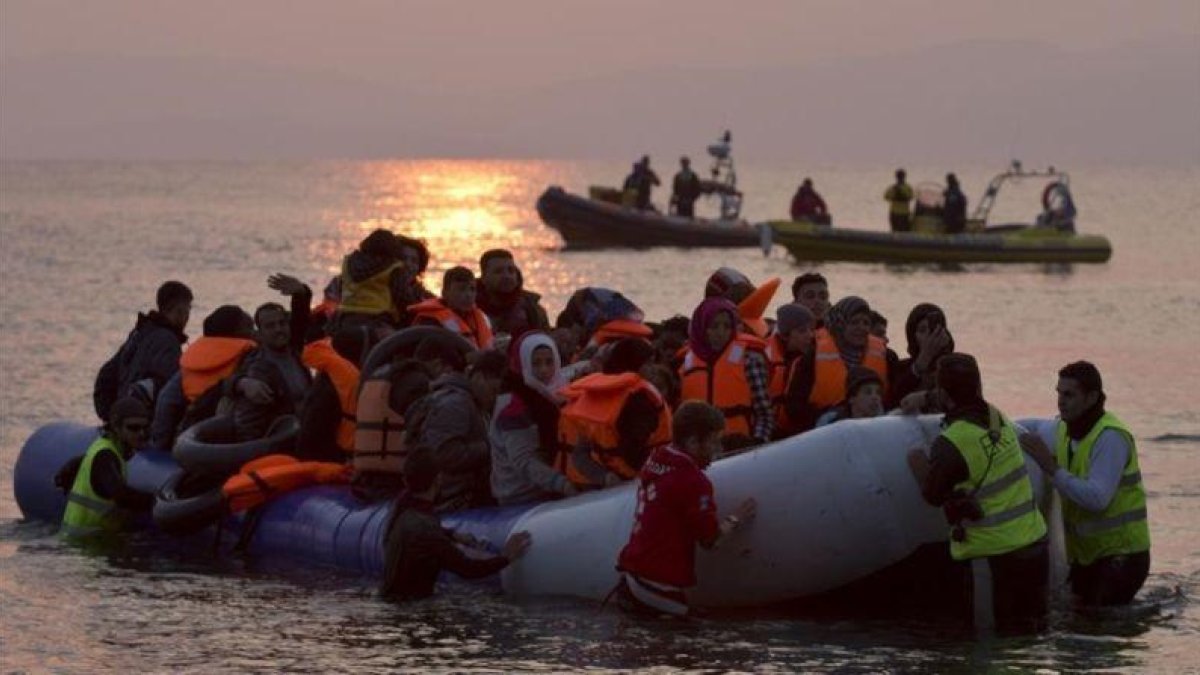 Varios voluntarios ayudan a refugiados a su llegada en un atestado bote neumático a Lesbos, el 20 de marzo.-AP / PETROS GIANNAKOURIS