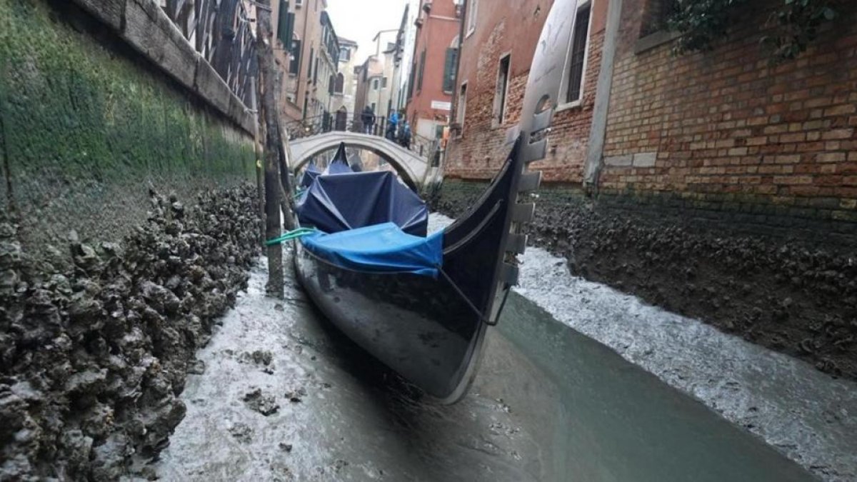 Una gondola permanece amarrada en un canal practicamente sin agua en Venecia.-ANDREA MEROLA