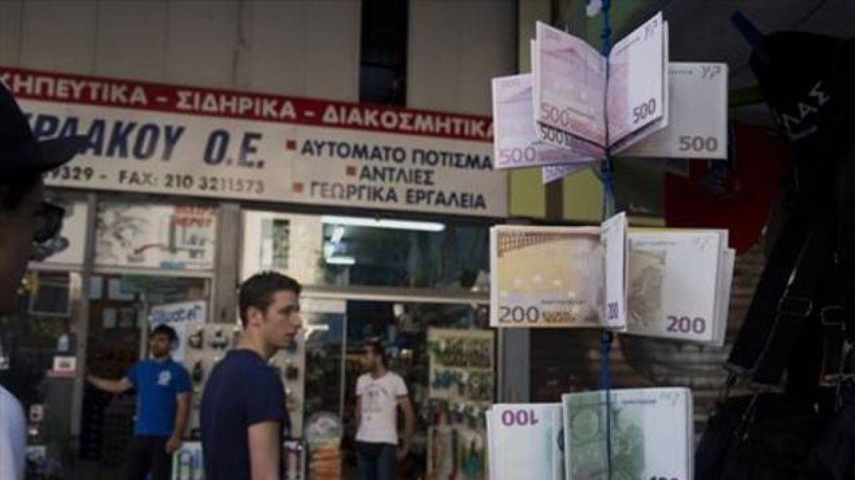Ciudadanos griegos pasean ante carteras con el diseño del euro en un quiosco del centro de Atenas, este martes.-
