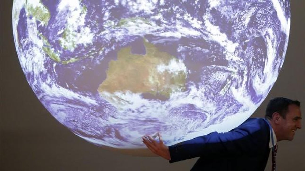 Un participante en la cumbre del clima posa ante la bola del mundo que se exhibe en el encuentro-REUTERS / STEPHANE MAHE