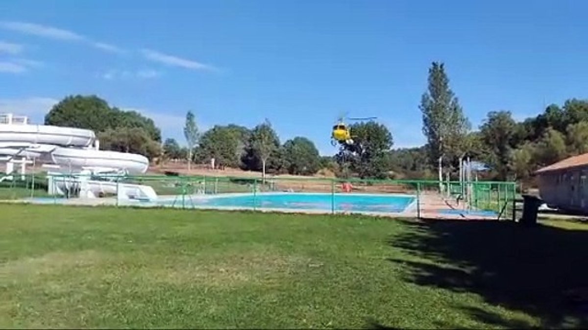 Un helicóptero carga agua en la piscina de Navaleno, previamente desalojada, para sofocar un incendio en la zona.