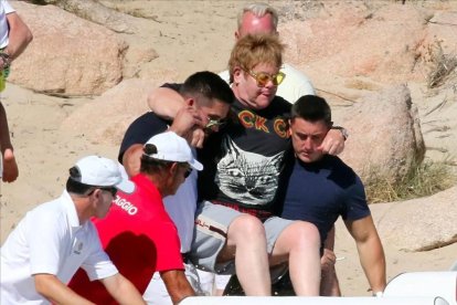 Elton John, cogido en volandas por sus guardaespaldas en la playa de Porto Cervo, en la isla de Cerdeña.-GTRES