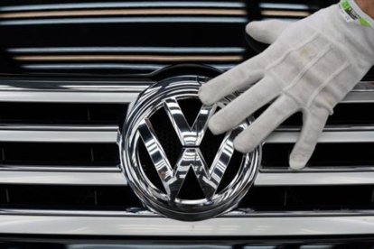 Un empleado coloca el logotipo de Volkswagen a un vehículo.-AFP / RALF HIRSCHBERGER