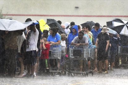 Un grupo de personas hace cola bajo una intensa lluvia en una tienda de ultramarinos en Carolina del Norte.-AP/ CHUCK LIDDY