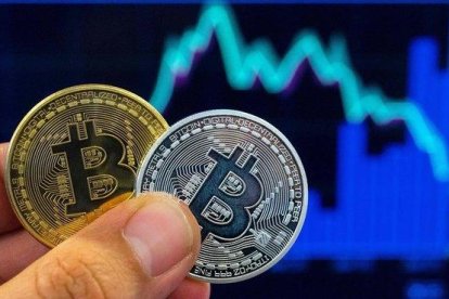 Una persona con dos representaciones físicas del Bitcoin.-AFP