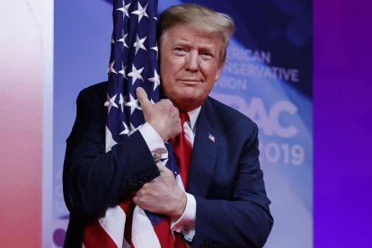 El presidente Donald Trump abraza la bandera de Estados Unidos en la Conferencia de Acción Política Conservadora.-AP / CAROLYN KASTER