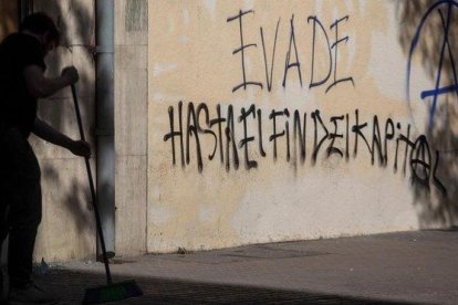 Un hombre barre el suelo ante un grafiti que reivindica la ’evasión’, en una calle de Santiago de Chile.-CLAUDIO REYES (AFP)