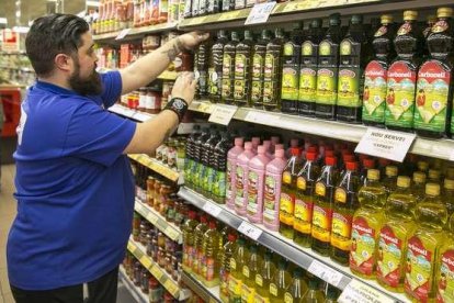 Un trabajador ordenando las botellas de aceite en un supermercado.-JOAN CORTADELLAS