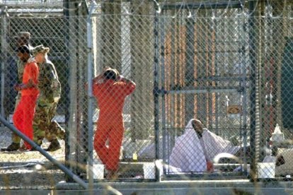 Un recluso de Guantánamo, escoltado por dos guardias en el penal, junto a otros dos presos en sus celdas, el 15 de marzo del 2002.-AP / TOMAS VAN HOUTRYVE