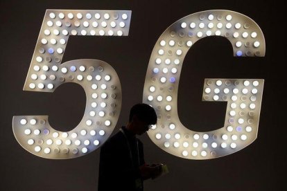 Un visitante usa su teléfono junto a un cartel de 5G en el estand de Intel.-JOSEP LAGO (AFP)