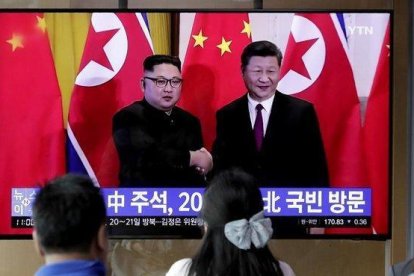 Unos transeúntes observan un programa de TV en el que aparecen el presidente chino Xi Jinping saludando al líder norcoreano Kim Jong-un en Pionyang.-LEE JIN-MAN (AP)