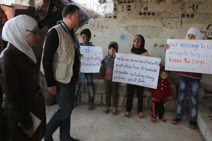 Niños sirios sostienen pancartas reivindicativas frente a miembros de un convoy de ayuda humanitaria durante una entrega de material en Al-Nashabia, en la región de Guta Oriental, al este de Damasco, el 28 de noviembre.-AFP / AMER ALMOHIBANY