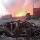 Vista de un coche calcinado en la seria de explosiones de unos almacenes de Tianjin, en China. En segundo plano, el fuego sigue ardiendo.-AFP / TIANJIN