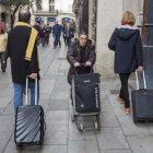 Una mujer pasa con su carrito de la compra entre dos turistas con sus maletas.-FERRAN NADEU