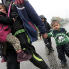 Un hombre camina llevando a dos niños bajo la lluvia junto a la frontera con Eslovenia.-SRDJAN ZIVULOVIC / REUTERS