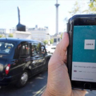 Un taxi de Londres pasa delante de un móvil con la aplicación de Uber activada, ayer.-REUTERS / TOBY MELVILLE