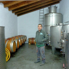 Santos Gómez en el interior de la bodega, junto a unos depósitos de acero inoxidable y unas barricas de roble. Abajo, podando una viña.-TST