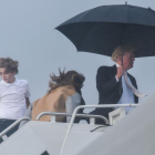 El presidente de EEUU, Donald Trump, sostiene un amplio paraguas para protegerse de la lluvia, mientras espera a su mujer Melania y a su hijo Barron, durante el embarque del Air Force One en Flordia.-/ AFP / NICHOLAS KAMM (AFP)
