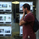 Un joven mirando ofertas de pisos de alquiler en los expositores de una inmobiliaria de Barcelona.-ELISENDA PONS