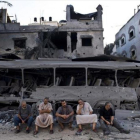 Cinco palestinos de Gaza sentados frente a un autobús y un edificio destruidos, en el 2014, por ataques aéreos israelís.-AFP / ROBERTO SCHMIDT