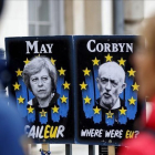 Unos peatones pasan junto a carteles con la primera ministra británica, Theresa May, y el líder del Partido Laborista, Jeremy Corbyn, cerca del Parlamento, en Londres.-TOLGA AKMEN (AFP)