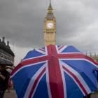 Un transeúnte se refugia de la lluvia en un paraguas con la bandera británica, cerca del Big Ben.-AFP / JUSTIN TALLIS