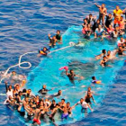 Momento del rescate de los migrantes que esperan sobre el casco de la embarcación.-