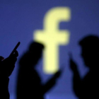 Unos usuarios de Facebook, ante el logotipo de la red social.-DADO RUVIC / REUTERS
