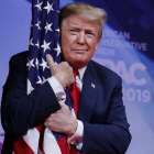 El presidente Donald Trump abraza la bandera de Estados Unidos en la Conferencia de Acción Política Conservadora.-AP / CAROLYN KASTER