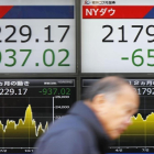 Un hombre pasa ante un cartel que exhibe las pérdidas del índice Nikkei, a la izquierda, y del Dow Jones, en una firma de valores en Tokio-YOHEI FUKAI (AP)