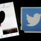Un usuario de Twitter lee mensajes de esta red social en el móvil frente al logo del pájaro, símbolo de la misma.-/ REUTERS / REGIS DUVIGNAU