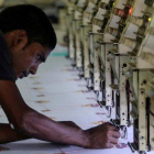 Un trabajador indio ajusta una máquina de coser en un planta de Bombai (India).-