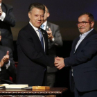 Santos (izquierda) y Rodrigo Londoño, alias 'Timochenko', se dan la mano tras firmar el nuevo acuerdo, en Bogotá, este jueves.-AP / FERNANDO VERGARA