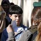 Un nino palestino muestra su carnet de identidad a una agente israelí mientras espera para poder cruzar a Jerusalen a través del puesto de control de Belén.-ABED AL HASHLAMOUN