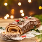 Tronco de Navidad decorado con chocolate, acebo y frutos rojos sobre mesa rústica navideña